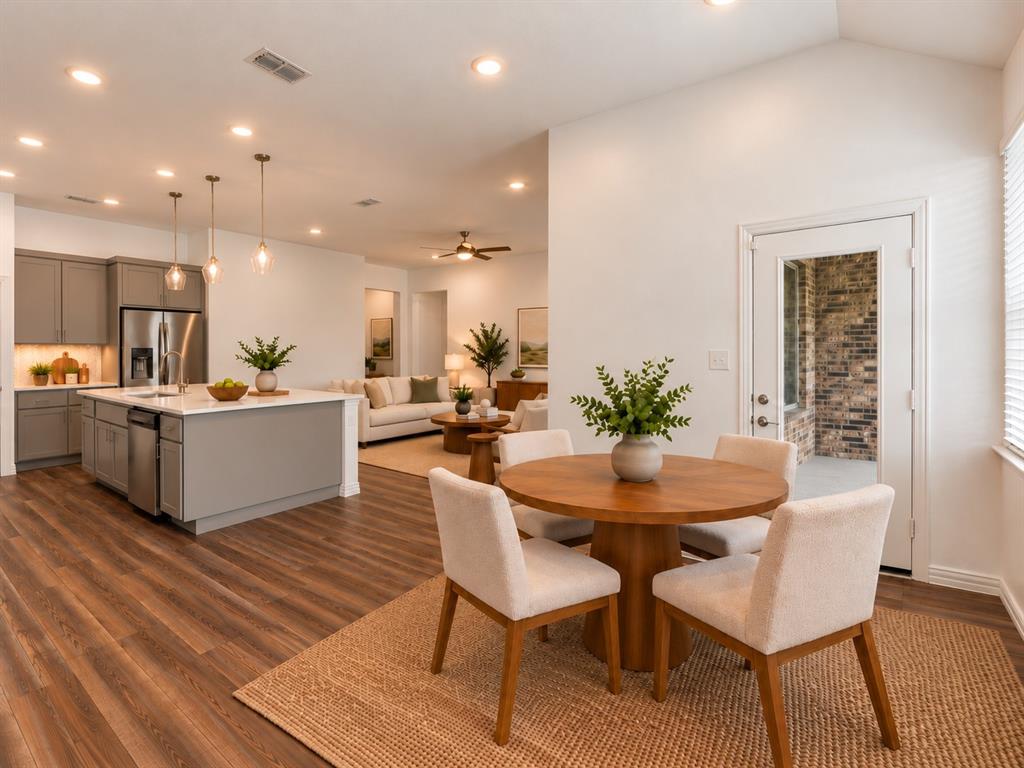 Open kitchen featuring a central island, neutral-toned cabinetry, stainless steel appliances, and wood-finish flooring throughout. Virtual photo
