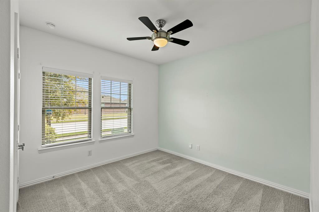 Neutral-toned carpeted flooring, two double-pane windows with horizontal blinds, and a central ceiling fan with integrated lighting