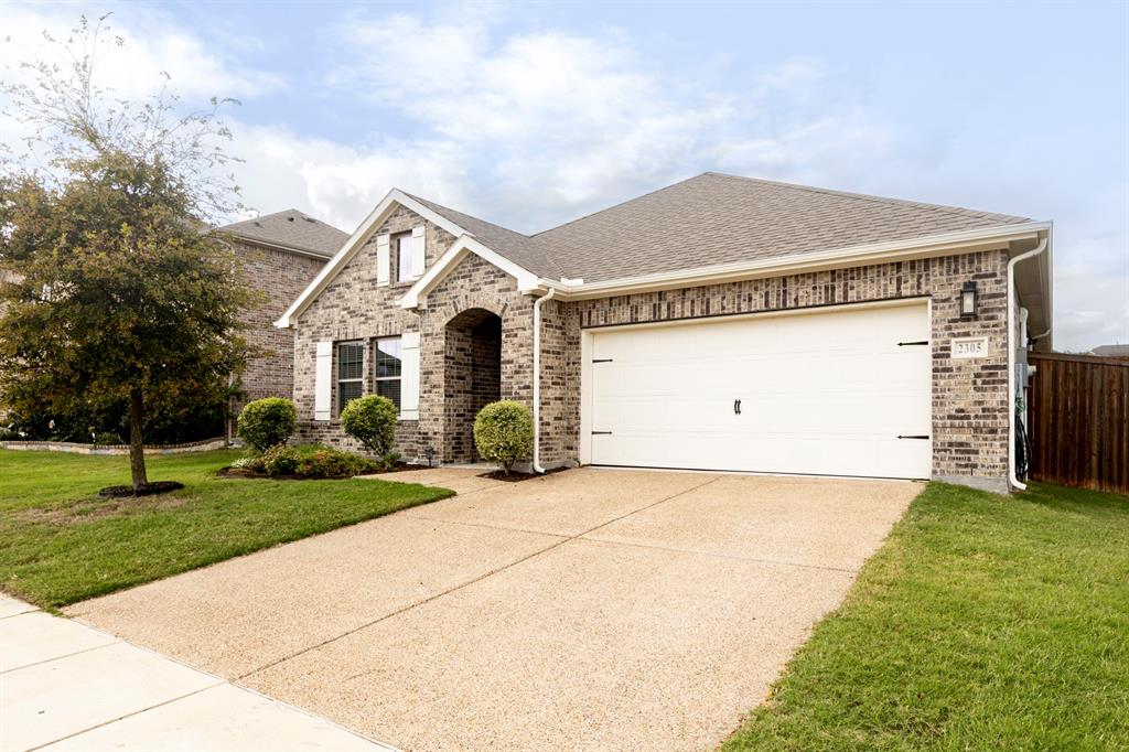 Brick exterior residence featuring a front-facing attached garage, arched entryway, white shutter accents, and a concrete driveway