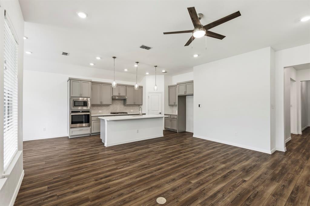 Kitchen featuring wood-finish flooring, grey shaker-style cabinetry, white center island, built-in double oven, and recessed ceiling lighting