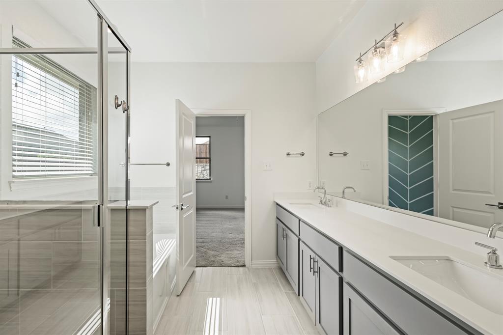 Bathroom featuring a dual-sink vanity with solid-surface countertops, a glass-enclosed shower with tile surround, an oversized wall-to-wall mirror, and neutral tile flooring