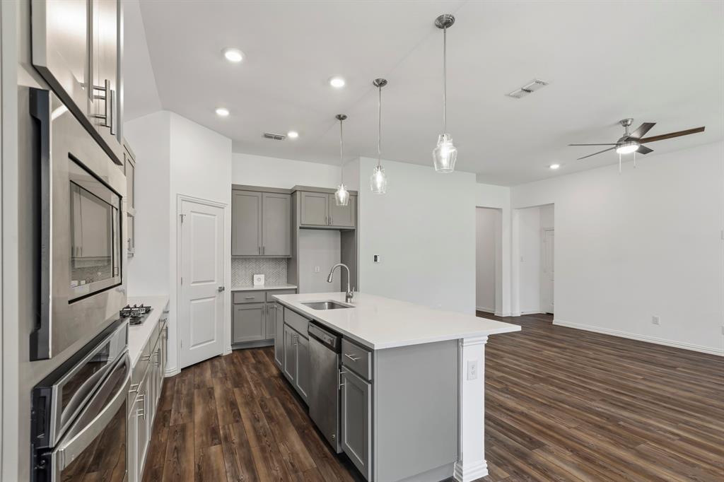 Kitchen featuring grey cabinetry, a central island with a solid-surface countertop, stainless steel appliances, pendant lighting, and wood-finish flooring