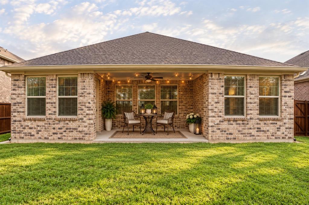 Rear exterior featuring a brick facade, covered patio, integrated ceiling fan, recessed lighting, and manicured lawn