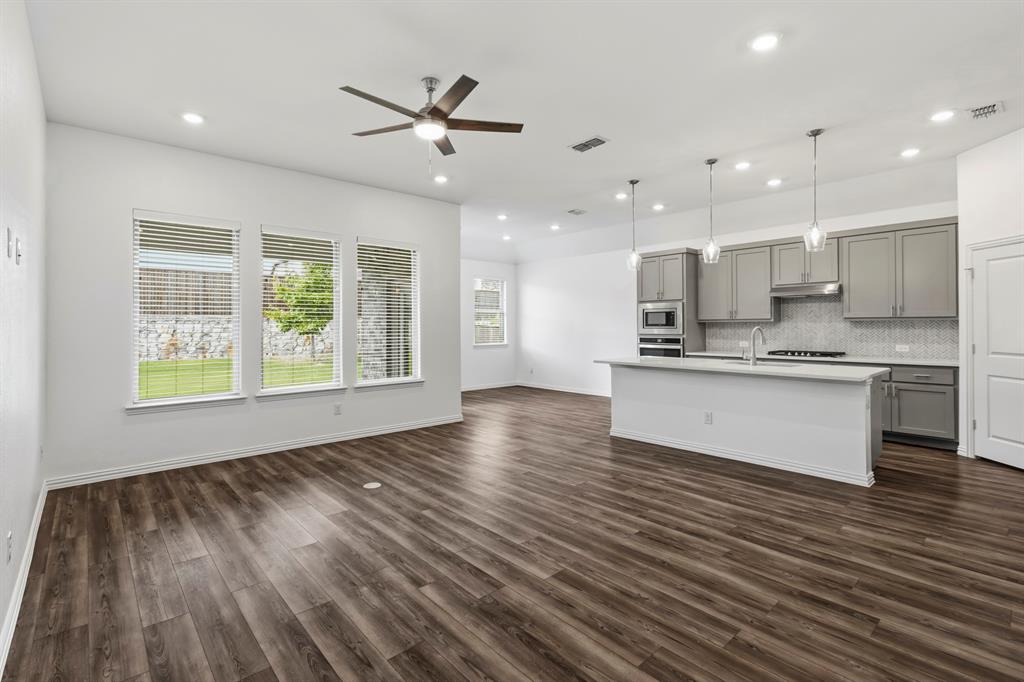 Open-concept area featuring wood-finish flooring, a kitchen island with stone countertops, gray cabinetry, recessed lighting, and pendant fixtures