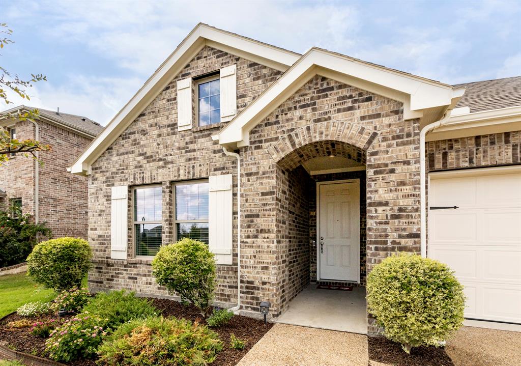 Brick exterior featuring a gabled roofline, arched covered entryway, decorative white shutters, and a concrete walkway