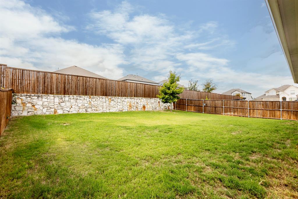 Backyard featuring a leveled lawn, natural stone retaining wall, and full-perimeter wood fencing