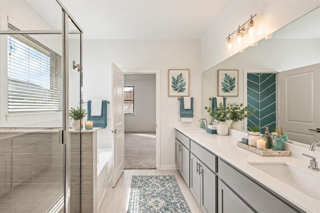 Bathroom featuring a dual-sink vanity with stone countertop, frameless glass-enclosed shower, soaking tub, and wall-to-wall mirror with four-light fixture