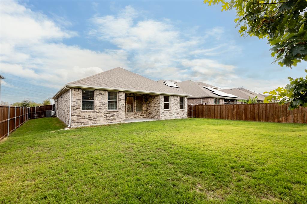 Brick exterior featuring a covered patio, gabled roofline, and wood privacy fencing enclosing a lawn