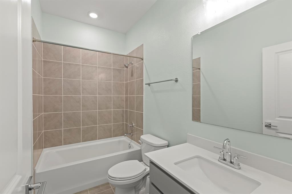 Bathroom featuring a white vanity with a composite countertop, an integrated rectangular sink, a shower-tub combination with tiled surround, and a wall-mounted mirror