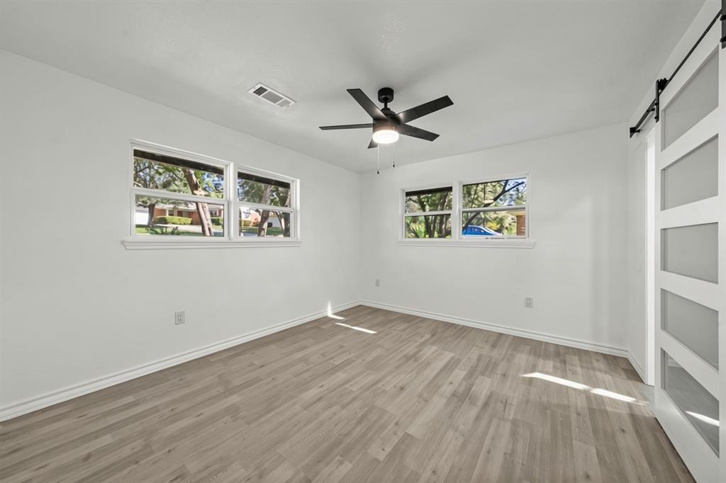 Interior space featuring wood-finish flooring, a ceiling fan with integrated lighting, dual-pane windows, and a white sliding barn door with frosted glass panels