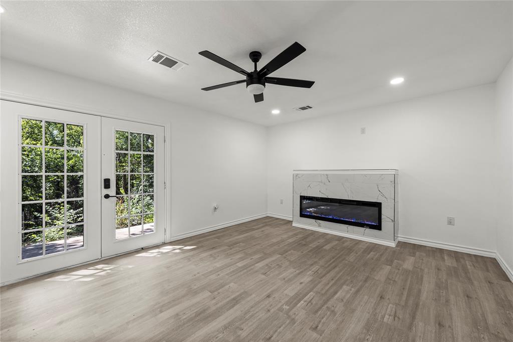 Wood-finish flooring, recessed lighting, matte black ceiling fan, dual-pane French doors, and built-in electric fireplace with stone-pattern surround