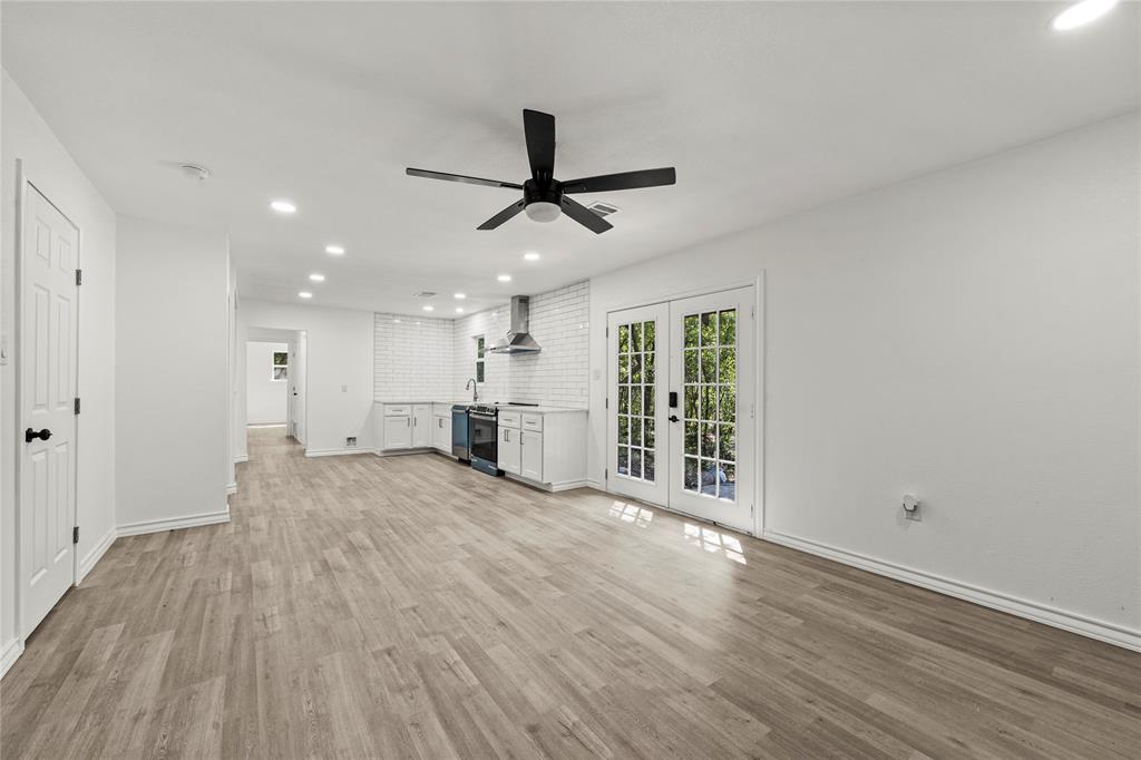 Open-concept interior featuring wood-finish flooring, recessed lighting, white subway tile kitchen backsplash, stainless steel range hood, and double glass-pane doors