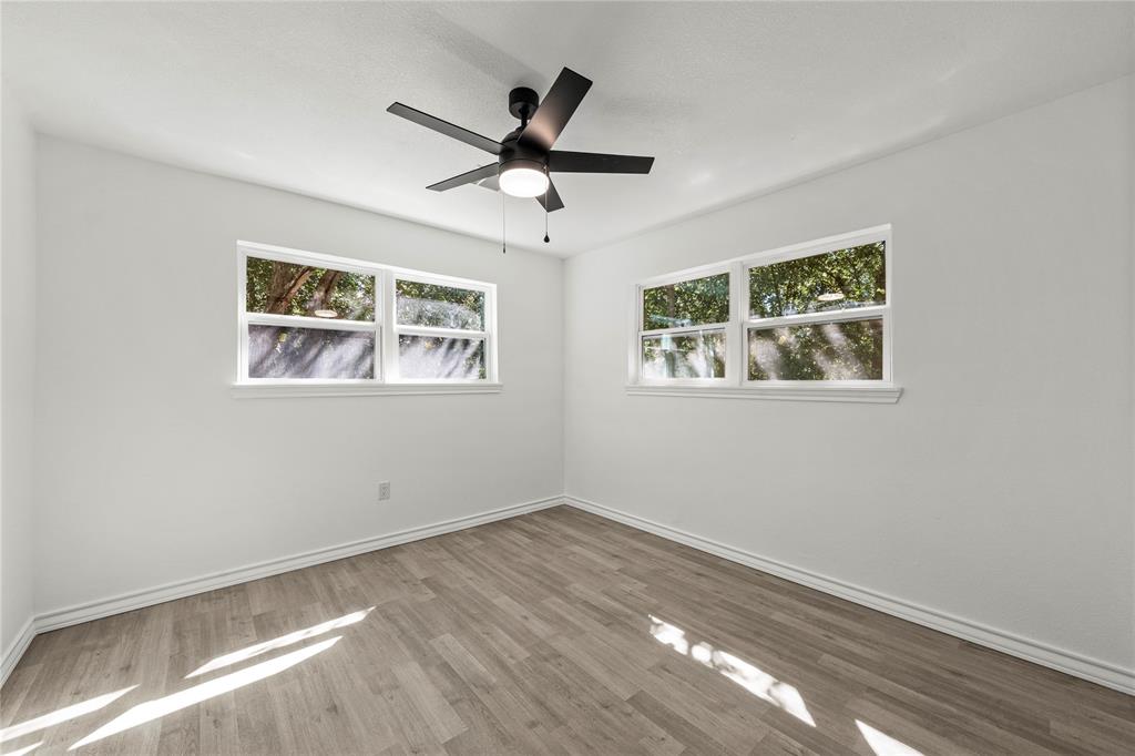 Neutral interior featuring light-toned wood-finish flooring, white walls, and a modern ceiling fan with integrated lighting, complemented by dual windows
