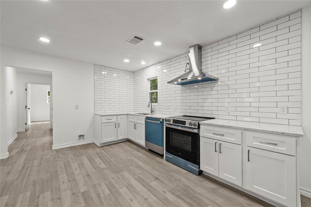 Kitchen featuring white shaker-style cabinetry, stone-finish countertops, full-height white subway tile backsplash, stainless steel range hood, and wood-finish flooring