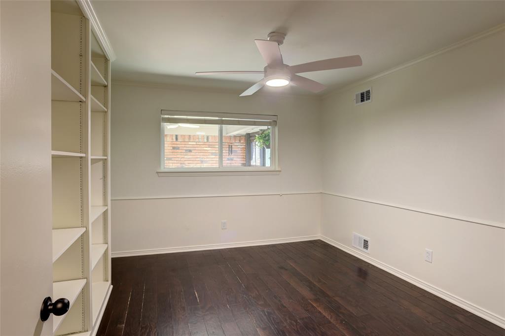 Interior room featuring dark wood-finish flooring, built-in shelving, white wainscoting, and a ceiling fan with integrated lighting
