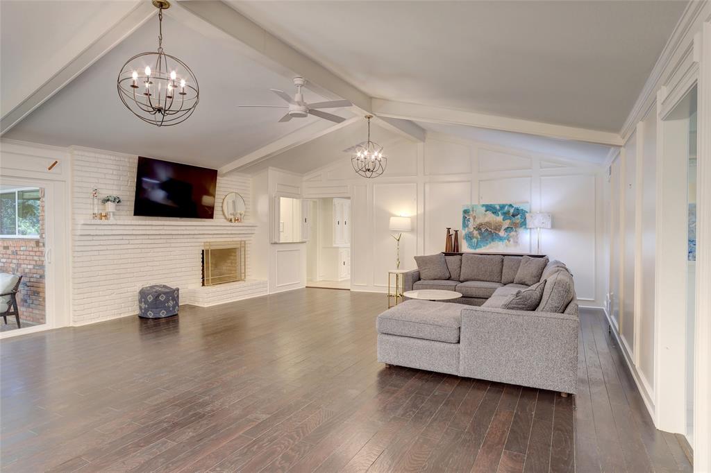 Vaulted ceilings with exposed beams, wood-finish flooring, painted brick fireplace, and dual spherical chandeliers
