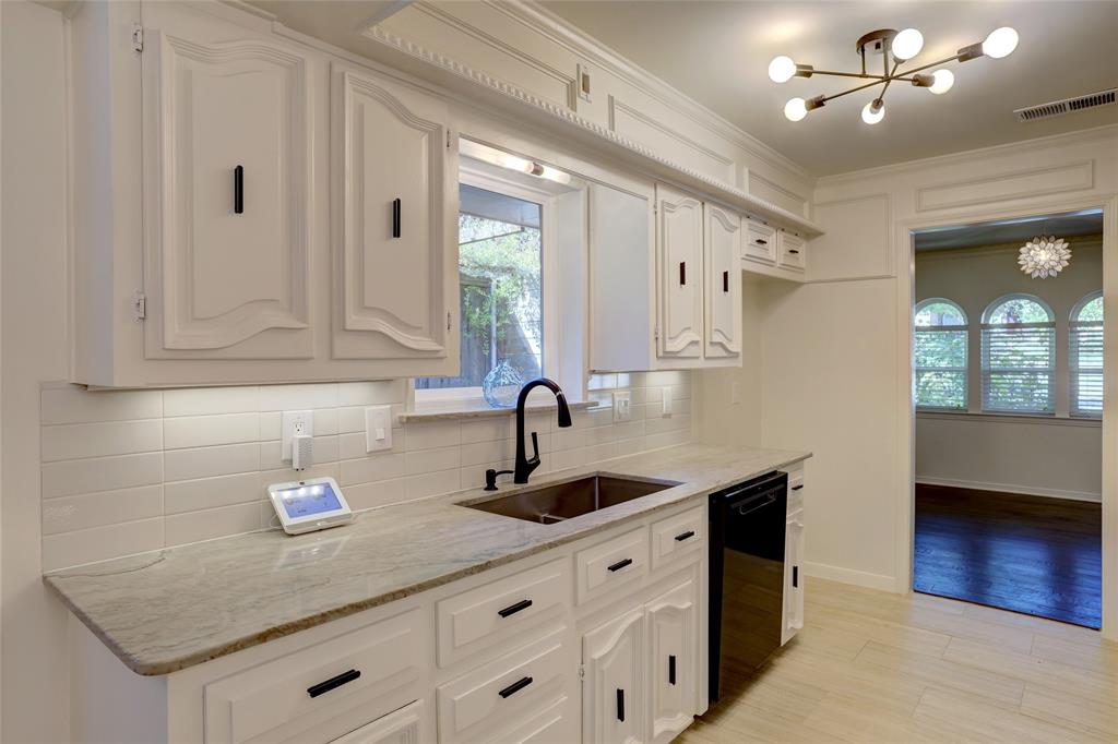 Custom white cabinetry with black hardware, stone countertops, subway tile backsplash, stainless steel undermount sink, and contemporary multi-arm ceiling fixture