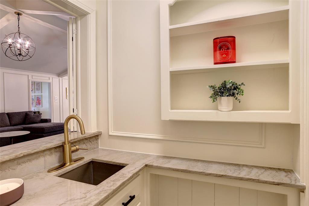 Built-in recessed shelving, stone countertop, undermount sink with brass-finish faucet, and wainscoting detail