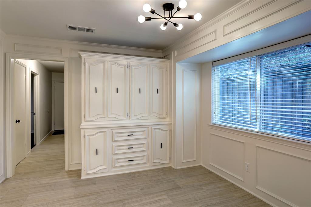 Built-in cabinetry featuring white raised-panel doors and drawers, contemporary multi-arm light fixture, wood-finish flooring, and decorative wall paneling