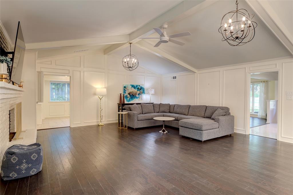 Vaulted ceilings featuring decorative beams, wood-finish flooring, wainscoting wall paneling, a painted brick fireplace surround, and spherical metal chandeliers