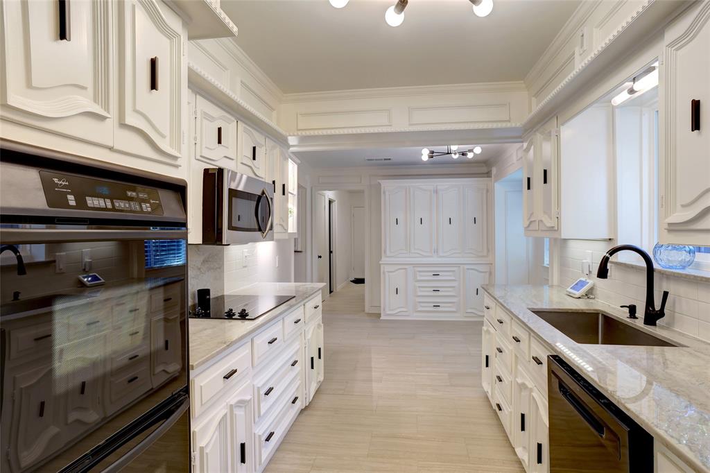 Kitchen featuring white custom cabinetry with matte black hardware, stone countertops, stainless steel wall-mounted oven and microwave, tiled backsplash, and wood-finish flooring