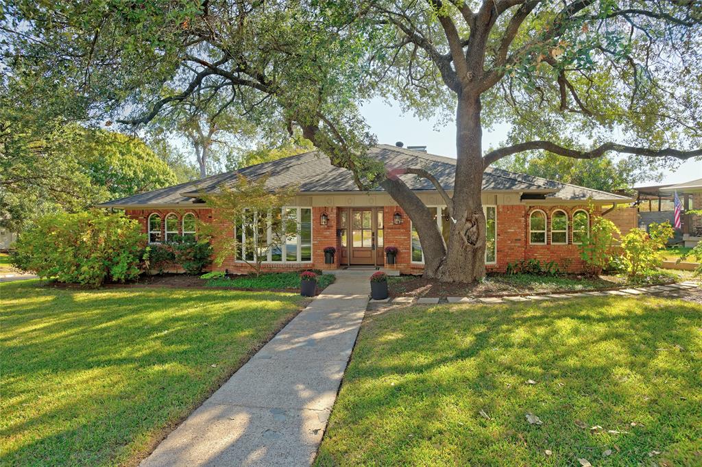 Brick exterior featuring a hip roofline, arch-top windows, multi-pane bay windows, and a mature oak tree