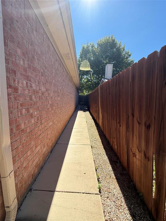 Exterior side yard featuring a brick facade, concrete walkway, and a vertical wood privacy fence