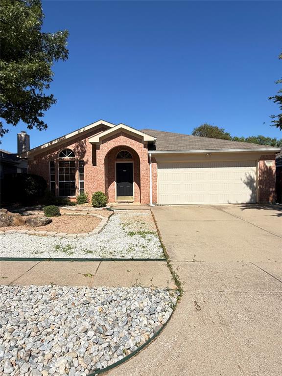 Single-story brick exterior featuring a recessed arched entryway, covered two-car garage, multi-pane window with an arched transom, and stone-accented landscaping