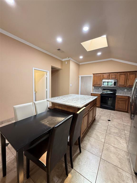 Kitchen featuring a central island with a stone-finish countertop, recessed lighting, vaulted ceiling, skylight, and ceramic tile flooring