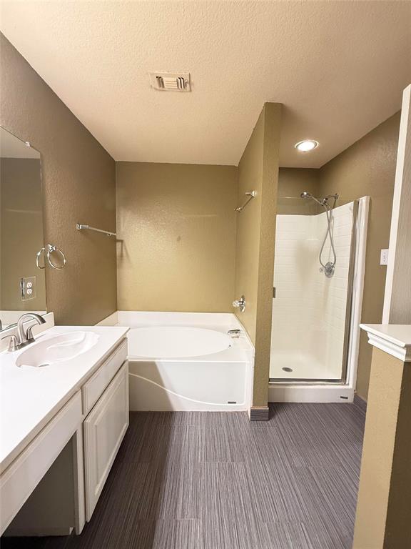 Bathroom featuring a white vanity with integrated sink, oversized soaking tub, separate shower stall with a glass door, and linear-patterned wood-finish flooring