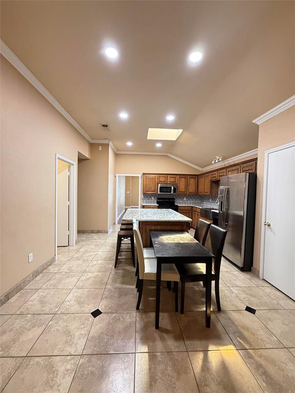 Kitchen featuring a central island with a stone-finish countertop, recessed lighting, vaulted ceiling with a skylight, tile flooring with decorative inserts, and wood cabinetry