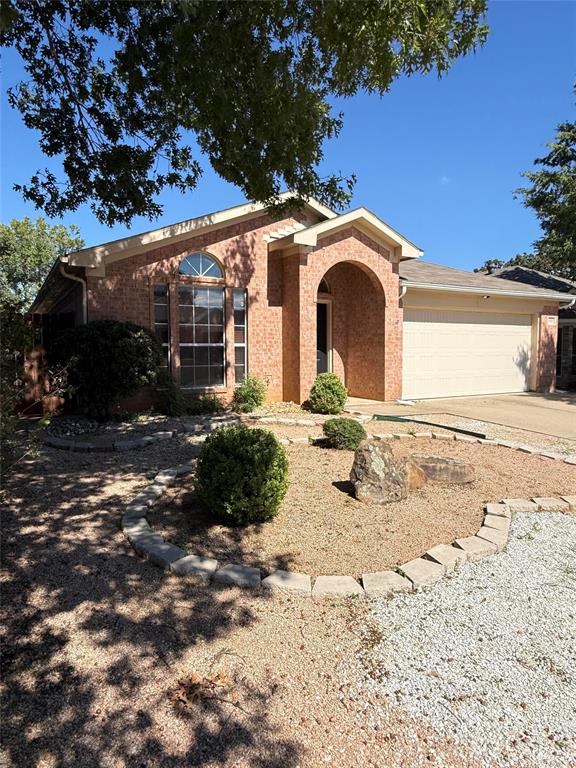 Brick exterior featuring an arched entryway, decorative stone-lined landscaping, and an attached two-car garage