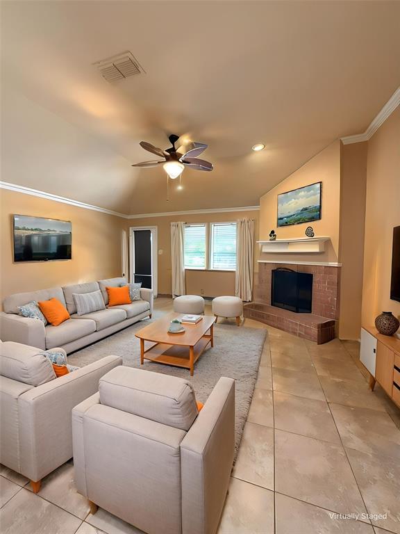 Vaulted ceiling featuring a central lighted ceiling fan, masonry fireplace with a tiled hearth and mantel, and large-format tile flooring