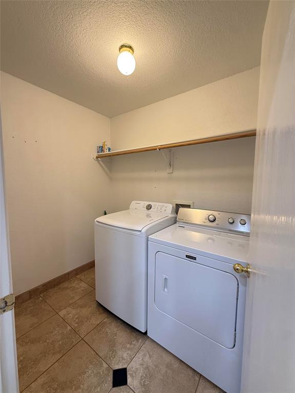 Dedicated laundry area featuring tile flooring, a mounted wood-finish shelf, and a globe-style flush mount ceiling light