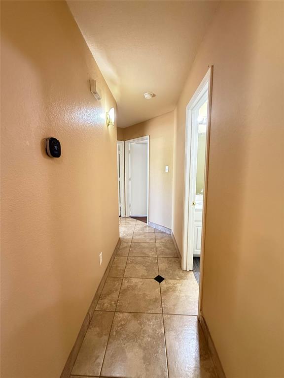 Hallway featuring square stone-finish tile flooring with decorative black accents, wall-mounted digital thermostat, and recessed lighting