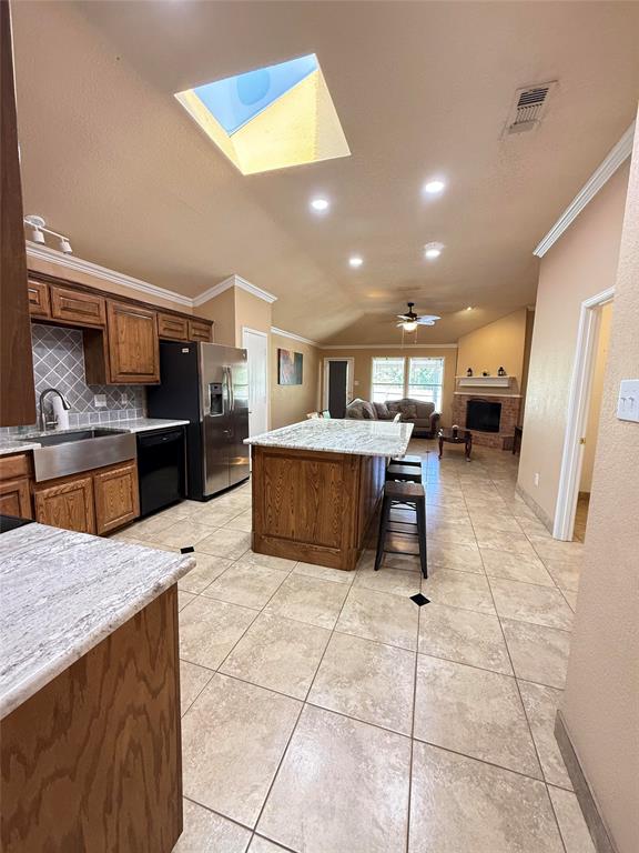 Kitchen featuring a central island with stone countertop, stainless steel apron-front sink, patterned tile backsplash, recessed lighting, and a vaulted ceiling with skylight