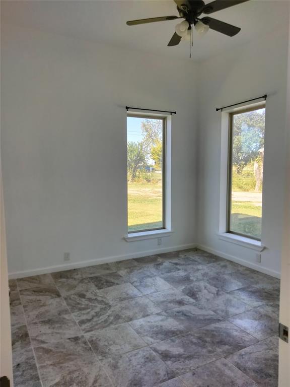 Interior space featuring large-format tile flooring, high ceilings, two tall windows with curtain rods, and a ceiling-mounted light fixture with a fan