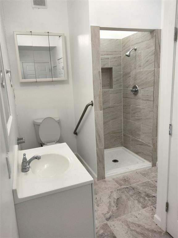 Bathroom featuring a white vanity with an integrated sink, stone-finish floor tiling, a walk-in shower with neutral wall tiling and a built-in shower niche, and a wall-mounted medicine cabinet