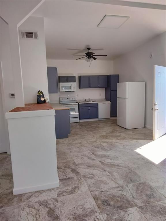 Kitchen featuring blue cabinetry, stone-finish tile flooring, integrated white appliances, and a ceiling-mounted fan