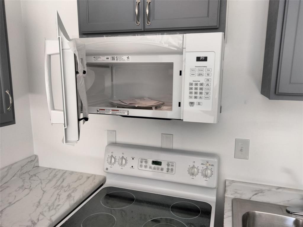 Built-in over-the-range microwave, white electric range with four-burner cooktop, gray shaker-style cabinetry, and stone-finish laminate countertops
