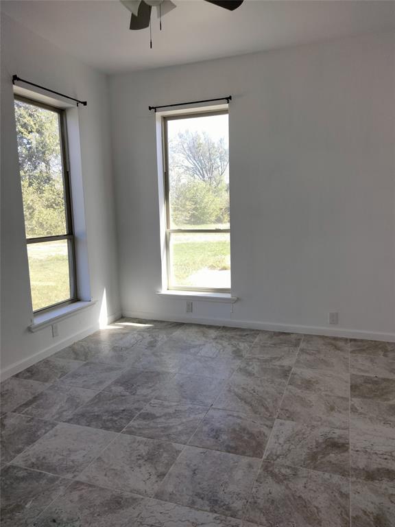 Neutral-toned stone tile flooring, dual full-height windows, and ceiling fan fixture