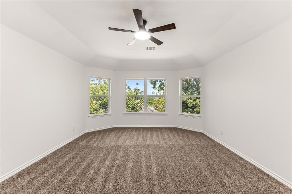 Room featuring a tray ceiling, triple-window bay configuration, wall-to-wall carpeting, and a central ceiling fan with an integrated light fixture