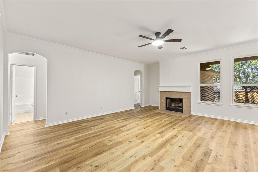 Spacious room featuring wood-finish flooring, a fireplace with a stone-surround hearth, two arched doorways, and a ceiling-mounted light fixture with a fan