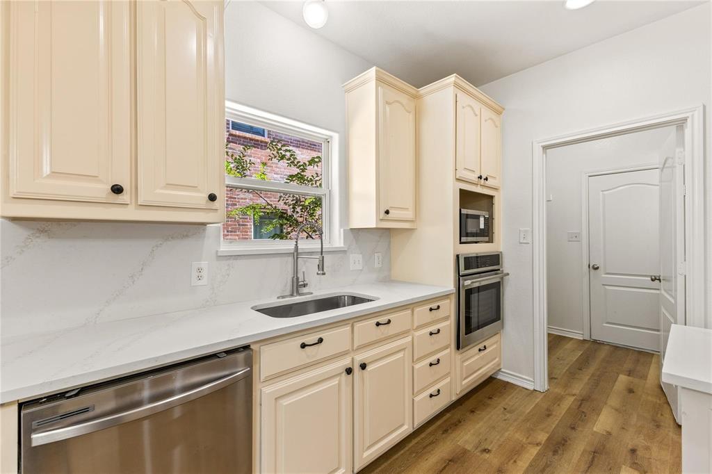 Kitchen featuring light-toned cabinetry, solid surface countertops with matching backsplash, stainless steel sink with high-arch faucet, integrated wall oven and microwave, and wood-finish flooring