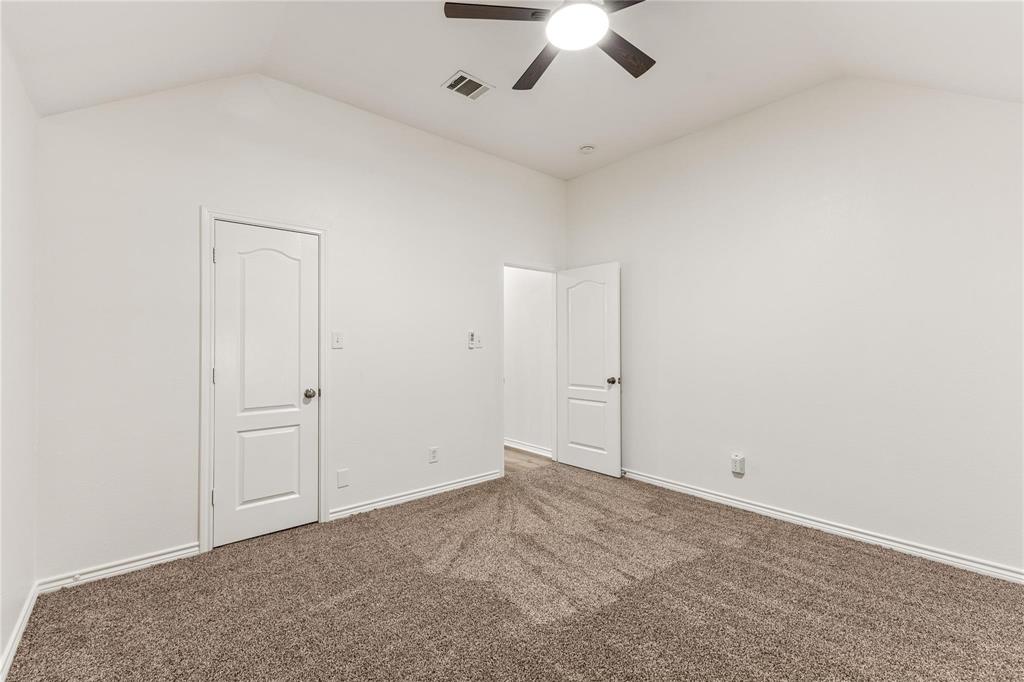 Vaulted ceiling featuring a central lighted ceiling fan, neutral wall-to-wall carpeting, and two interior doors with arched-panel detailing