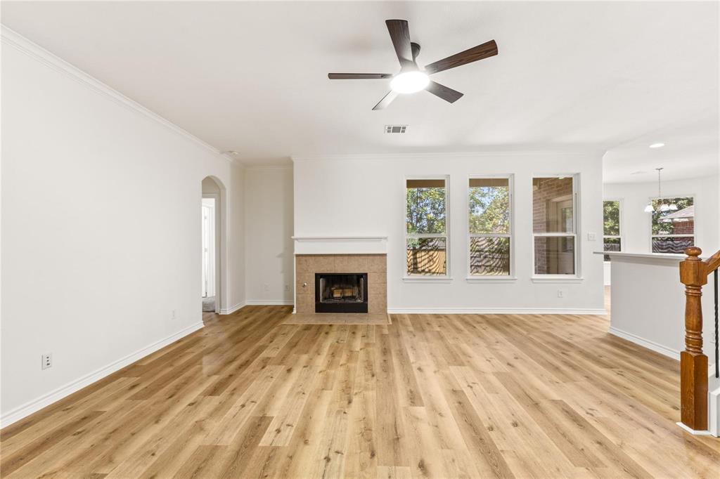 Open floor plan featuring wood-finish flooring, a fireplace with a neutral-toned tile surround, a multi-blade ceiling fan with integrated lighting, and large windows