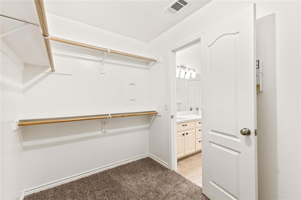 Walk-in closet featuring tiered wood shelving and rods, neutral carpeting, and a raised-panel interior door