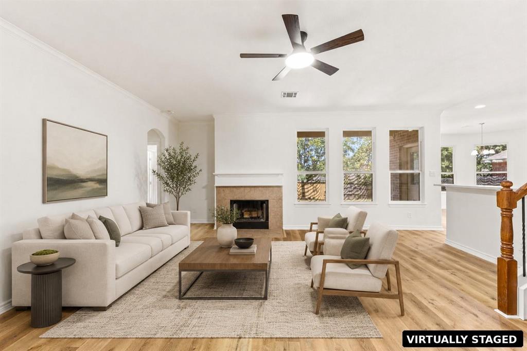 Living area featuring wood-finish flooring, a fireplace with a neutral tile surround, a ceiling fan with integrated lighting, and multiple tall windows