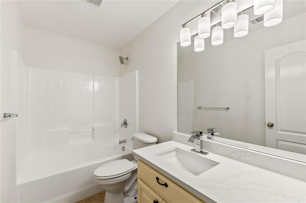 Bathroom featuring a vanity with a white composite countertop, an integrated rectangular sink, a multi-bulb light fixture, a large wall-mounted mirror, and a tub-shower combination with tiled surround