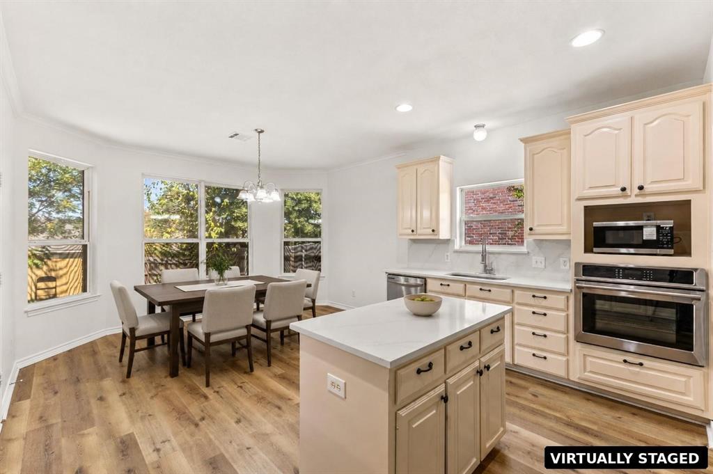 Kitchen featuring light-toned cabinetry, stone-surface countertops, center island, built-in stainless steel oven and microwave, and wood-finish flooring